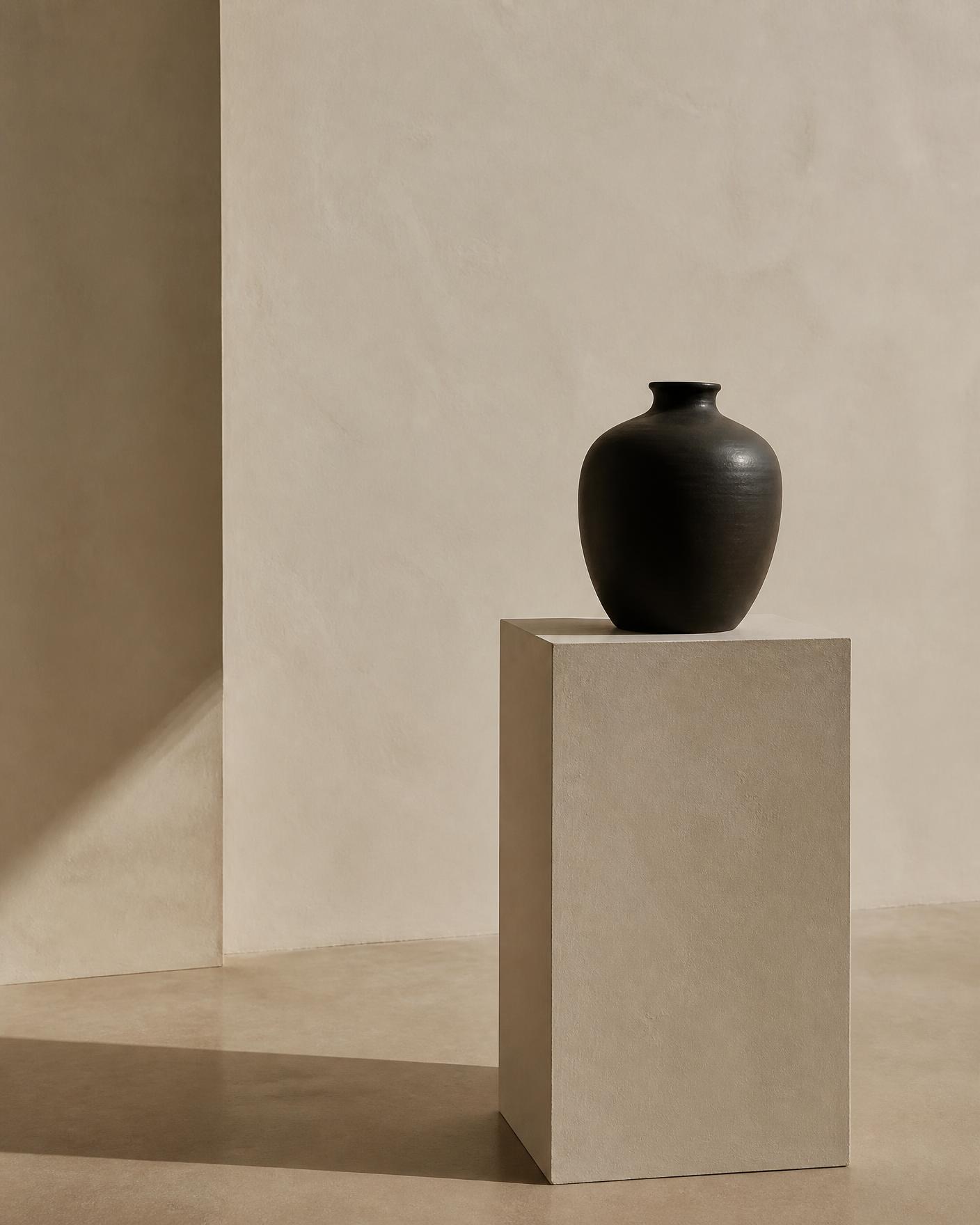 Dark ceramic vessel on a plaster pedestal in an empty room